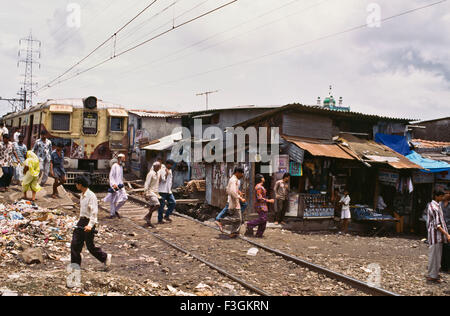 Passage à niveau ligne de chemin de fer de banlieue suburban train passe stretch dense avec des bidonvilles le long de son côté à Govandi gare Mumbai Banque D'Images