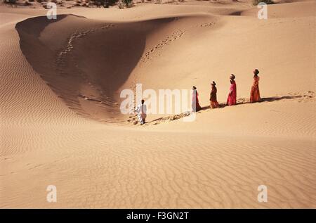 Les femmes Rajasthani transportent de l'eau pots et man playing drum marche dans le sable ; Khuhri ; ; ; Inde Rajasthan Jaisalmer Banque D'Images