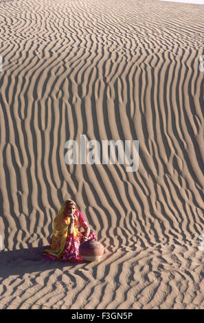 Femme assise avec Rajasthani attend quelqu'un dans l'argile pitcher dunes de sable modèle de couches en arrière-plan ; Bikaner Banque D'Images