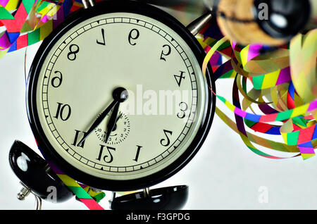Close up d'un réveil rétro noir, autour de minuit, avec des banderoles de papier et le liège d'une bouteille de vin mousseux, tête baissée Banque D'Images