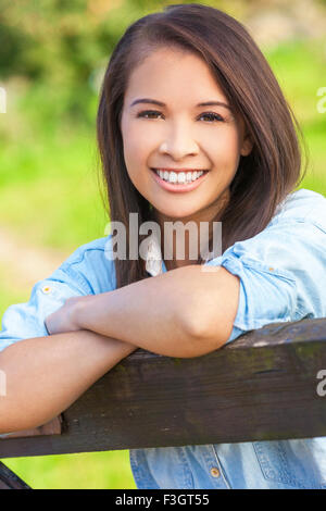 Belle jeune femme asiatique ou eurasienne girl wearing denim shirt, souriant et s'appuyant sur une clôture en sunshine Banque D'Images