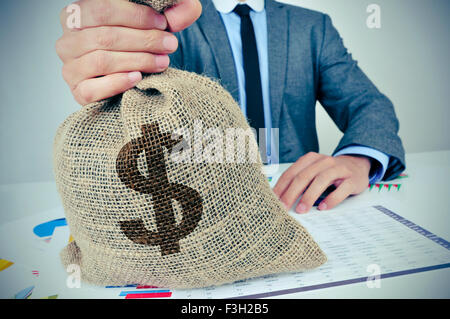 Un jeune homme de race blanche portant un costume gris assis à un bureau bureau plein de graphiques et les équilibres financiers détient un BA de l'argent de jute Banque D'Images