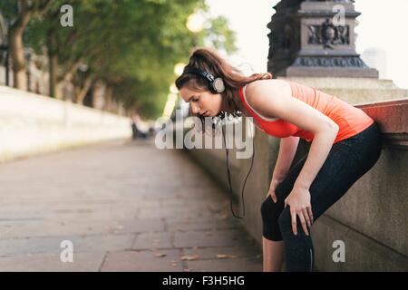 Jeune coureuse portant des écouteurs en faisant une pause sur Riverside Banque D'Images