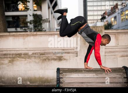 Jeune homme saute au-dessus de banc de parc en ville