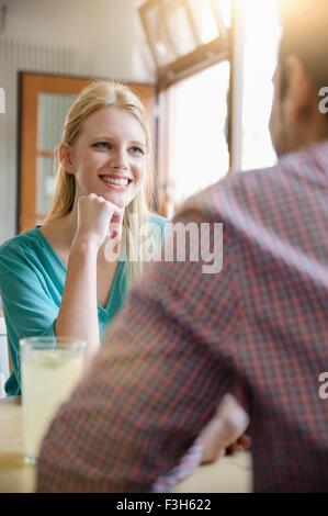 Au cours de l'épaule de young woman sitting with hand on chin looking at young man smiling
