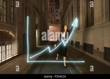 Businesswoman light painting tableau lumineux avec flèche vers le haut on city street at night Banque D'Images