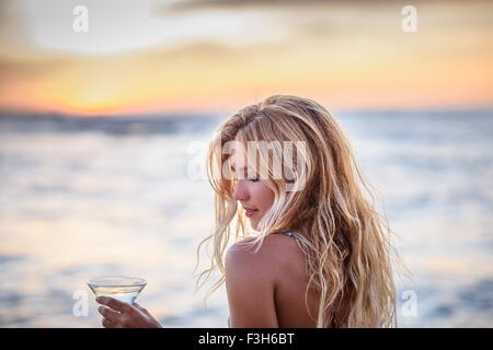 Young woman on beach drinking cocktail au coucher du soleil Banque D'Images