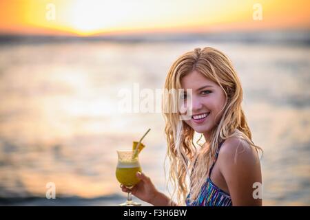 Portrait of young woman drinking cocktail sur la plage au coucher du soleil Banque D'Images