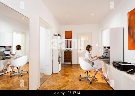 Mature businesswoman typing on laptop dans l'appartement Banque D'Images