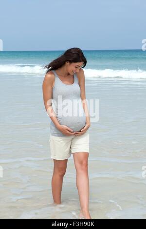 Pregnant woman paddling in sea avec les mains sur l'estomac Banque D'Images