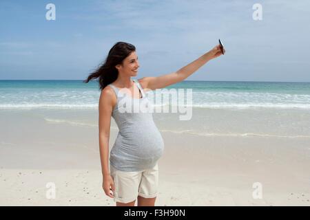 Enceinte Mid adult woman en tenant sur smartphone selfies at beach, Cap Vert, Afrique Banque D'Images