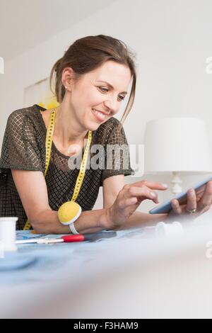 Woman ruban de mesure en appui sur les coudes using digital tablet smiling Banque D'Images