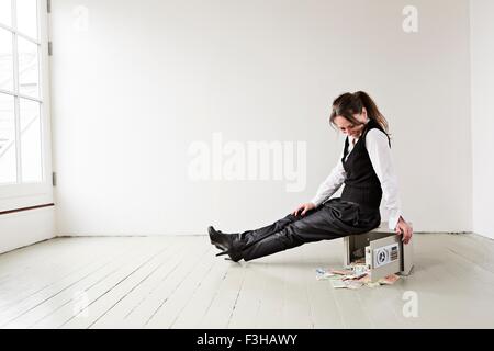 Mature Woman sitting on vide coffre-fort en chambre, coffre-fort porte ouverte avec de l'argent tomber Banque D'Images