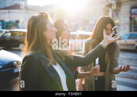 Trois jeunes femmes faisant des bulles on city street Banque D'Images