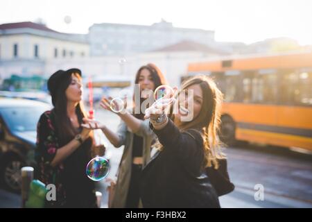 Trois jeunes amis féminins blowing bubbles on city street Banque D'Images