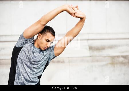 Young male runner se réchauffer avec les mains levées Banque D'Images