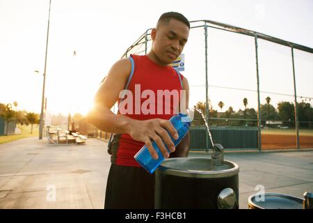 Jeune homme eau de remplissage bouteille de boissons fountain Banque D'Images
