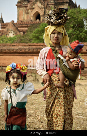 Jeune femme avec du bois sur sa tête et visage thanaka peindre avec ses enfants à Bagan, Mandalay, Myanmar Région Banque D'Images