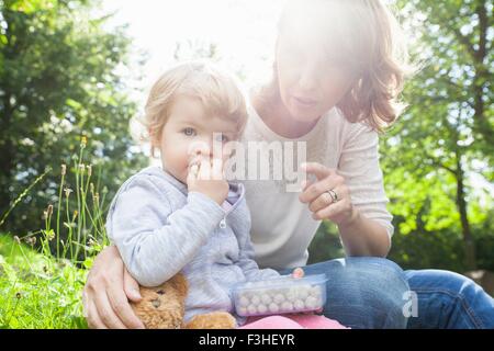 Mère et femme enfant manger des douceurs dans park Banque D'Images