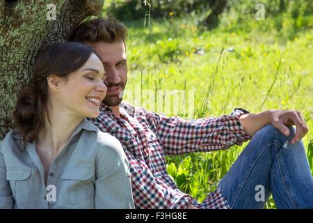 Young couple sitting leaning against tree ensemble Banque D'Images