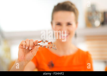 Gros plan sur young smiling woman holding dans la main d'un emporte-pièce en forme de chauve-souris pour Halloween des biscuits dans la cuisine. Aut traditionnels Banque D'Images