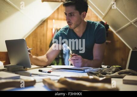 Young man leaning against workbench using digital tablet Banque D'Images