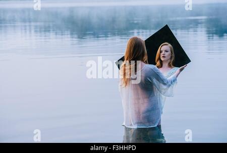 Vue arrière du jeune femme debout dans le lac Miroir à réflexion à tenir Banque D'Images