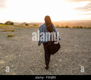 Vue arrière du jeune femme exerçant son étui à guitare au coucher du soleil Banque D'Images