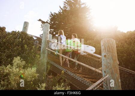 Couple walking up beach étapes, transportant des planches Banque D'Images