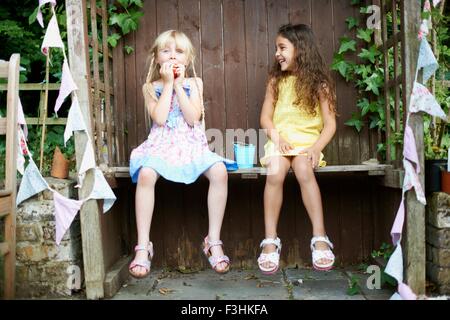 Portrait de deux jeunes filles assis sur un banc de manger un seau de fraises fraîches Banque D'Images