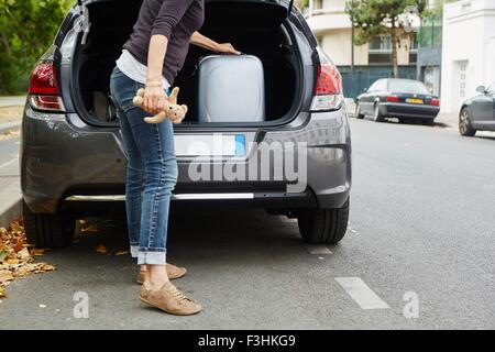 Femme debout à côté de voiture, mettre open boot valise Banque D'Images