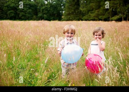 Frère et soeur dans l'herbe haute holding balloon looking at camera smiling Banque D'Images