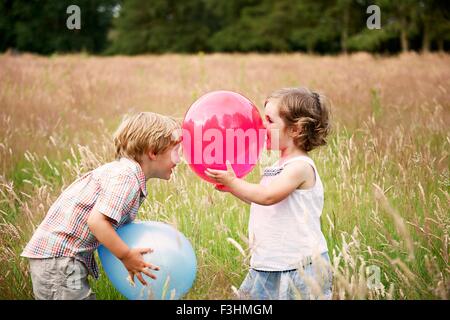 Frère et soeur dans l'herbe haute face à face jouer avec ballon Banque D'Images