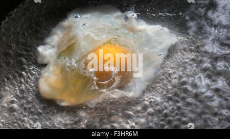 POÊLE À ŒUFS HUILE GROS PLAN sur l'œuf de poule frais bio en plein soleil en commençant à frire dans l'huile dans la poêle à frire de cuisine Banque D'Images