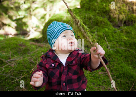 Un jeune garçon est titulaire d'une branche d'arbre qui est couvert de mousse verte. Banque D'Images