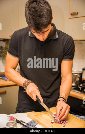 Jusqu'à la taille d'un jeune homme aux cheveux noirs, hacher l'oignon rouge avec un couteau dans la cuisine - Close Up de l'homme dans la cuisine, Ki Banque D'Images