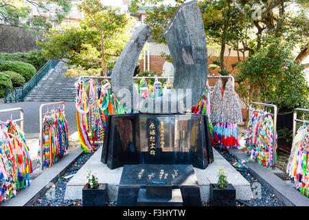 La bombe atomique de Nagasaki, parc de la paix. Grues de papier sur les bâtis autour d'une sculpture en mémoire de la mort. L'eau en bouteille laissée comme offrandes. Banque D'Images