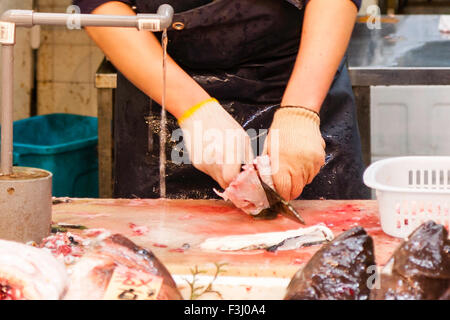 Japon, Osaka, Kuromon Ichiba Market, 'Osaka' Cuisine, homme, homme, mains seulement, de la détention et de l'éviscération du poisson-globe, fugu, sur planche de bois avec un grand couteau. Banque D'Images