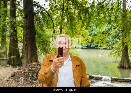 Veste en daim avec senior et chemise blanche dans un parc verdoyant selfies prend Banque D'Images