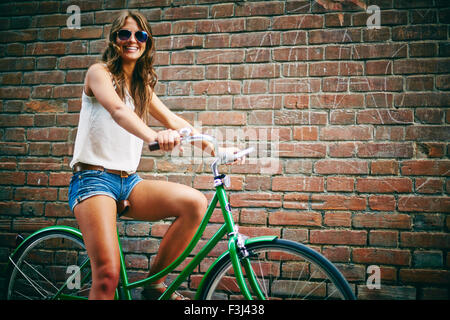 Lunettes cycliste féminine en se tenant contre un mur de briques Banque D'Images