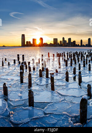 Pieux en bois de New York old pier qui sort à travers la glace, sur la Rivière Hudson au coucher du soleil avec des bâtiments de Jersey City Banque D'Images