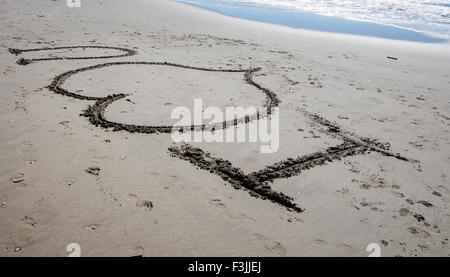 Je 'coeur' u écrit dans le sable d'une plage en France. Une vague se brise dans le coin supérieur droit. Le coeur symbolise l'amour. Banque D'Images