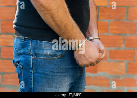 Arrestation, close-up shot man's hands avec des menottes en face de brique en terre cuite mur de blocs, côté droit Banque D'Images