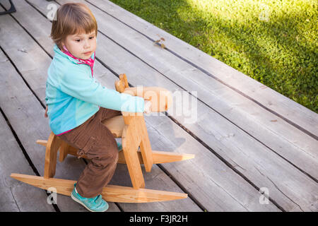 Outdoor portrait of cute young girl riding blond bébé jouet cheval de bois Banque D'Images