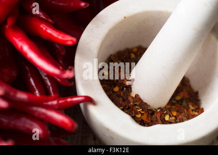 Chaud de flocons de piment rouge broyé dans un mortier et un pilon et poivrons frais. Banque D'Images