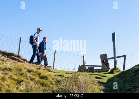 Randonnées dans la campagne anglaise. Les promeneurs marchant sur une colline vers un stile sur la grande crête, Derbyshire Peak District, England, UK Banque D'Images