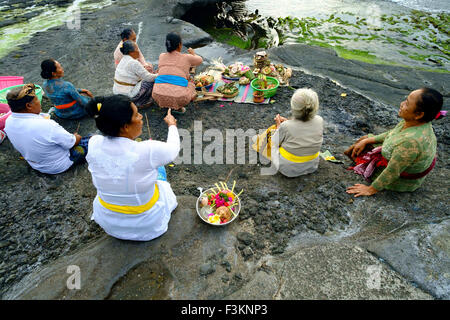 Les dévots hindous balinais prier au coucher du soleil sur les plages rocheuses autour du temple de Tanah Lot. Banque D'Images