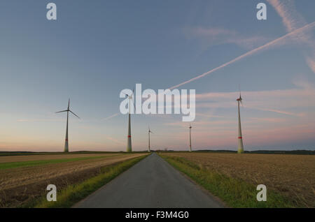 Cinq éoliennes à côté d'une petite route en agriculture paysage après le coucher du soleil Banque D'Images