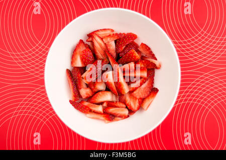 Freshly sliced fraises hachées et dans un bol blanc contre un fond texturé lumineux Banque D'Images