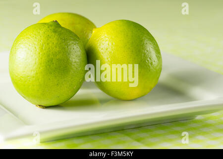 Limes vert frais sur une plaque blanche sur un fond vert estival et nappe à carreaux Banque D'Images